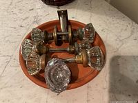 Top view of four vintage glass door knobs with brass bases arranged on a round terracotta plate, showing varied faceted glass designs.