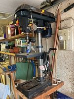 View of the full drill press showing the base, vertical column, adjustable table, and motor housing with control handles.