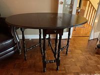 Front view of wooden drop-leaf table with both leaves extended, showing turned legs and drawer.