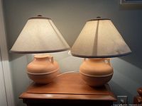 Pair of terracotta-style ceramic base table lamps with beige fabric shades placed on a wooden table.