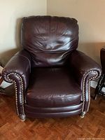 Front view of dark burgundy/brown leather recliner chair with rolled arms and nailhead trim, showing cushion creases and used condition.