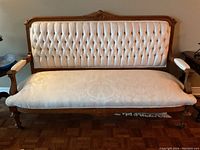 Full view of the antique love seat showing tufted upholstery, carved wood frame, and fabric seat cushion.