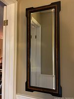 Full view of the tall rectangular mirror hung on a beige wall, showing its full shape and frame details.