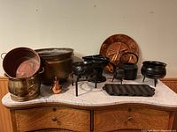 Wide view of iron pots, copper pots, trivet and copper decorative platter on marble surface