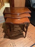 View of three nesting tables stacked on top of each other showing their size relationship and curved front edge detail with a medium brown wood finish.
