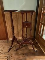 Shows both wooden plant stands side by side on wood floor against paneled wall.