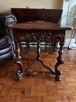 Front view of triangular wood table showing ornate scroll and floral carvings on apron and detailed curved legs.