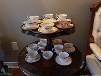 Top and bottom tier display of assorted vintage tea cups and saucers on a wooden stand, various floral and ornamental designs visible.
