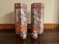 Front view of two hexagonal porcelain vases with traditional painted Chinese scenes and two small floral jars in front.