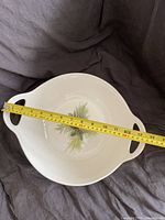 Top-down view of the white Christmas bowl showing a measuring tape across the diameter including handles, measuring about 20 inches wide.