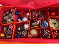 Top view of two sections of the red storage case filled with assorted Christmas tree decorations, including baubles and figurines.