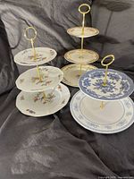 Three tiered platters showing floral and blue white porcelain plates with gold handles on dark fabric background