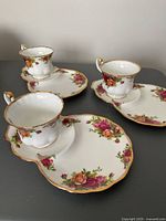 Three sets of vintage bone china tennis snack plates and cups with Old Country Rose floral pattern and gold trim arranged on a table.