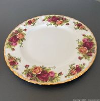 Close-up image of a single vintage Royal Albert Old Country Rose salad plate showing floral pattern and gold trim on a black surface.