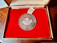 Obverse side of the silver medal showing the commemorative text and maple leaf with 'Canada 25'. Displayed in a red velvet-lined case.