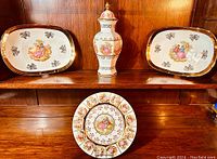 Photo of two rectangular platters and round cabinet plate displayed on wood shelf, all with gold rims and courting couple images.