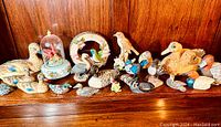 Wide view showing entire collection of various duck and bird figurines arranged on wooden shelf.