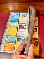 Open binder showing pages of Pokémon Trading Cards in clear plastic protective sleeves. Cards including Alolan Vulpix, Bunnelby, Pikachu, Noibat, Rhyhorn, and others are visible.