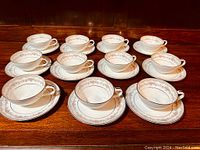 Wide shot of all 11 tea cups and saucers displayed together noting the design and condition.