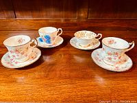 Four Paragon fine bone china tea cups with matching saucers in various floral patterns and gold trim on a wooden surface.