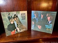 Two Rolling Stones vinyl LP album covers displayed side by side against wooden background: 'Big Hits (High Tide and Green Grass)' on left, '12 x 5' on right.