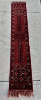 Full length view of the narrow handmade wool runner rug displaying the intricate geometric woven patterns primarily in red, black, and dark tones with fringes at the ends.