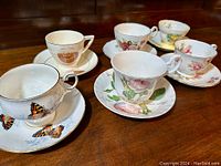 Set of six English fine bone china tea cups and saucers arranged on table showing variety of floral and decorative patterns.