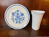 Figgjo dinner plate and white Kaiser vase side by side on wooden surface.