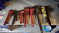All nine pipe wrenches arranged side by side on a table, showing various sizes and colors including red and yellow painted wrenches.