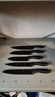 Five Cuisinart knives with black ergonomic handles and protective sheaths, laid out parallel with sheaths on.