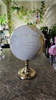 Front view of white globe with gold continents on brass stand, showing South Pacific Ocean text.