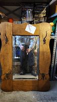Front view of wooden framed rectangular mirror with four metal hooks. Background shows storage items.