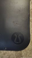 Close-up photo showing the embossed Lululemon logo on the black yoga mat surface.