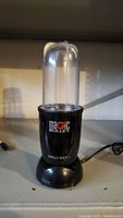 Photo of Magic Bullet Single Shot blender unit showing black base, clear blending cup, and power cord.