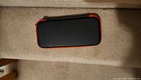 Closed black hard shell Nintendo Switch carrying case with red edging placed on carpet.