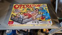 Front of the Operation board game box showing game title and artwork with patient on operating table.