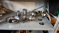 Photo of stainless steel dishes on shelf including two margarita glasses, teapot, gravy pourer, bowl, and other items.