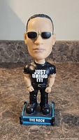 Front view of The Rock bobblehead figurine displaying sunglasses, 'Just Bring It!' shirt, and base with name plate.