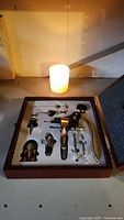Photo of the complete wine opener set with 9 pieces arranged inside a wooden box with foam padding.