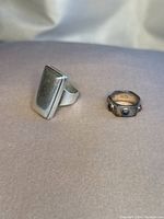 Photo of two silver rings, one rectangular faced solid silver ring and one square band ring with colored stones.