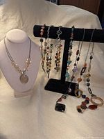Seven polished stone and glass necklaces displayed on a necklace stand and bust form showing variety of colors and shapes.
