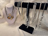 Main image showing eight vintage faux pearl necklaces displayed on black velvet jewelry stand and white bust. Various styles including single strand, cluster, and statement mixed media designs.