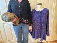 Person holding folded brown, beige, and gray knits with purple sweater displayed on mannequin