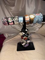 Seventeen vintage watches displayed on stand, showing variety in bands and dial designs including metallic, leather, and fabric bands.