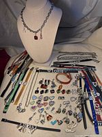 Wide photo showing six charm necklaces on a bust and dozens of charm bands and charms arranged on the surface.