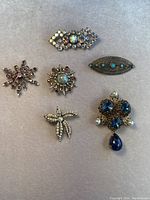 Overview of all six vintage pins laid out on fabric showing different styles and colors including rhinestones, pearls, and turquoise stones.
