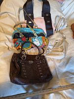 Photo showing all four vintage purses on a beige background, including brown studded handbag, multicolor handbag with robot charm, cream small backpack, and black bag with wide gold-accented strap
