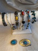 Overview of seven bracelets on display stand with two brooches in front