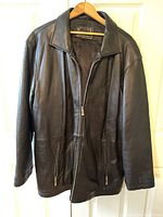 Front view of black leather Togo jacket with zip closure and zippered pockets on wooden hanger.