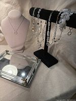 Mirrored vanity tray with six pieces of vintage jewelry displayed on black velvet bar and mannequin bust for scale.